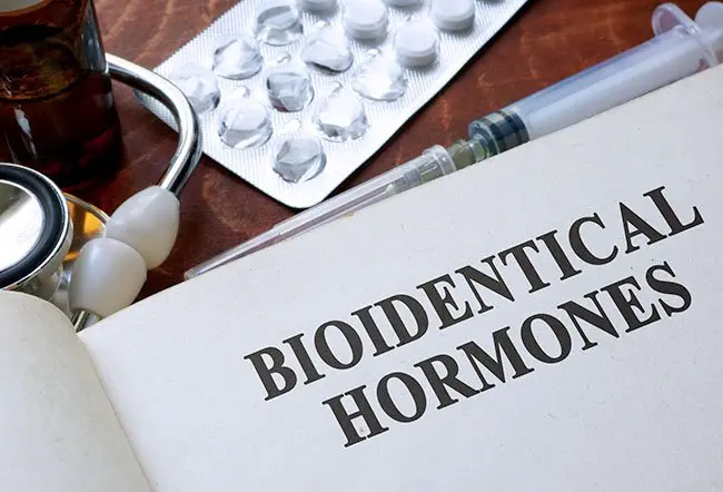 Bioidentical hormones reference book alongside a stethoscope, medication, and syringe